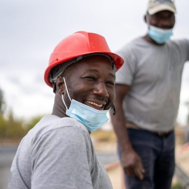 Two Afro-American builders wearing helmets and face masks while working